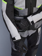 Veste Alpinestars Andes Air Drystar®, veste de touring moto, gris glace et gris foncé avec des accents jaune fluo, gros-plan montrant les panneaux en mesh et les sangles de réglage, portée avec des gants Alpinestars noirs