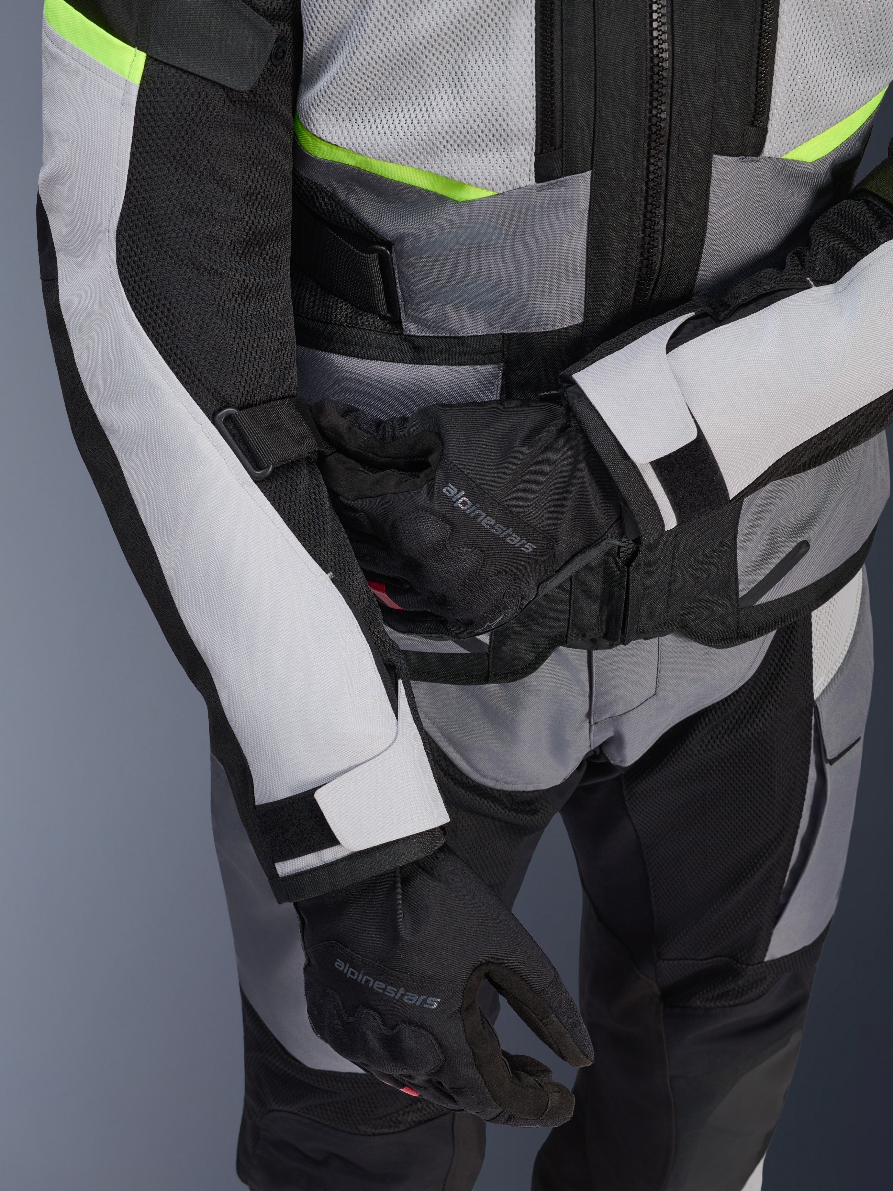 Veste Alpinestars Andes Air Drystar®, veste de touring moto, gris glace et gris foncé avec des accents jaune fluo, gros-plan montrant les panneaux en mesh et les sangles de réglage, portée avec des gants Alpinestars noirs