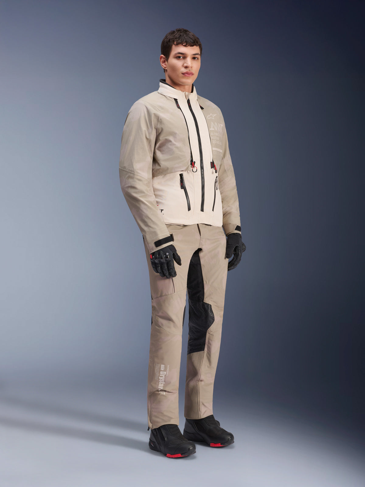 Veste Alpinestars AMT-10LAB Drystar® XF, veste de moto aventure, camouflage aluminium sable blanc, portée avec un pantalon d'aventure assorti, des gants et des bottes de moto noirs, photo de studio en pied, équipement de protection multi-saisons