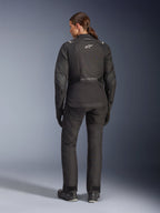 Motarde vue de dos portant la veste Alpinestars Stella Andes V4 Drystar® noire, associée à un pantalon de moto assorti, logo Astar blanc dans le dos, ourlet arrière allongé, tenue d'aventure-touring complète incluant gants et bottes noirs