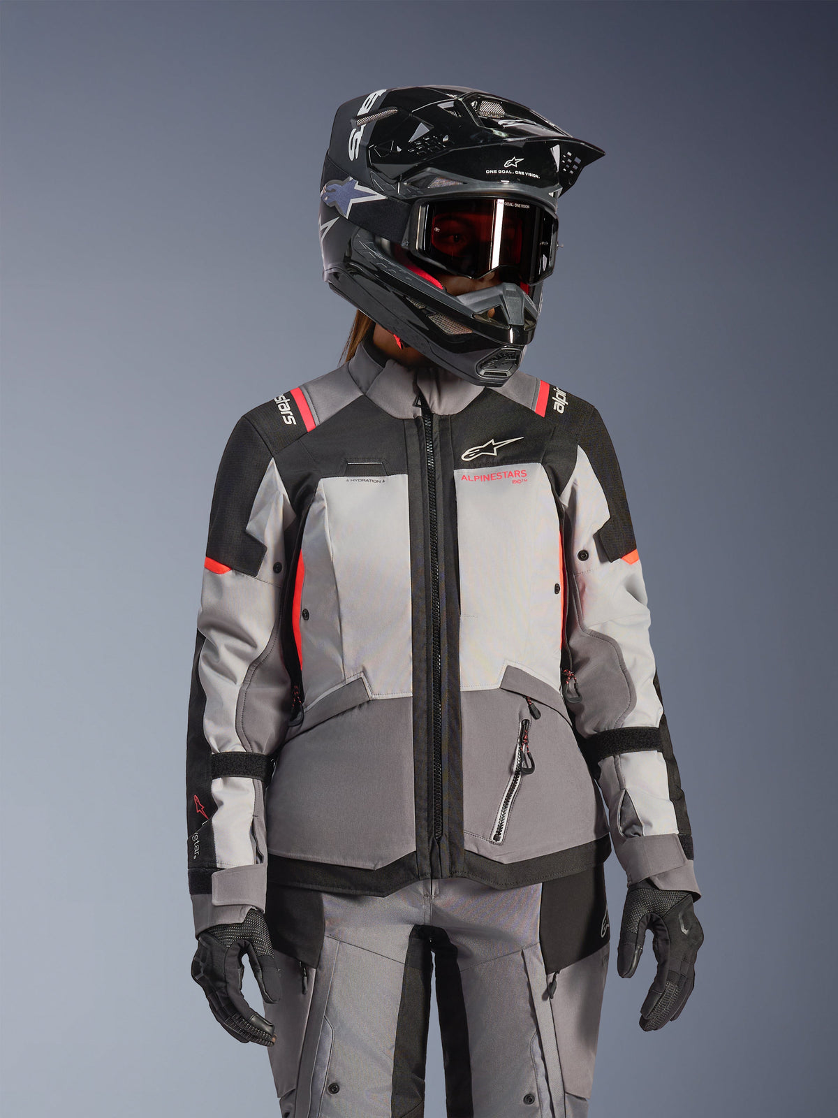 Veste Alpinestars Stella Andes V4 Drystar®, veste de moto adventure touring pour femme, grise et noire avec accents corail fluo, imperméable et respirante, portée avec un casque et des gants de protection