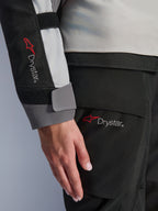 Détail en gros plan de la manche de la veste Stella Andes V4 Drystar® pour femme Alpinestars et du pantalon assorti, arborant le logo Drystar, construction textile gris glace et noir, marquage imperméable pour équipement de touring aventure