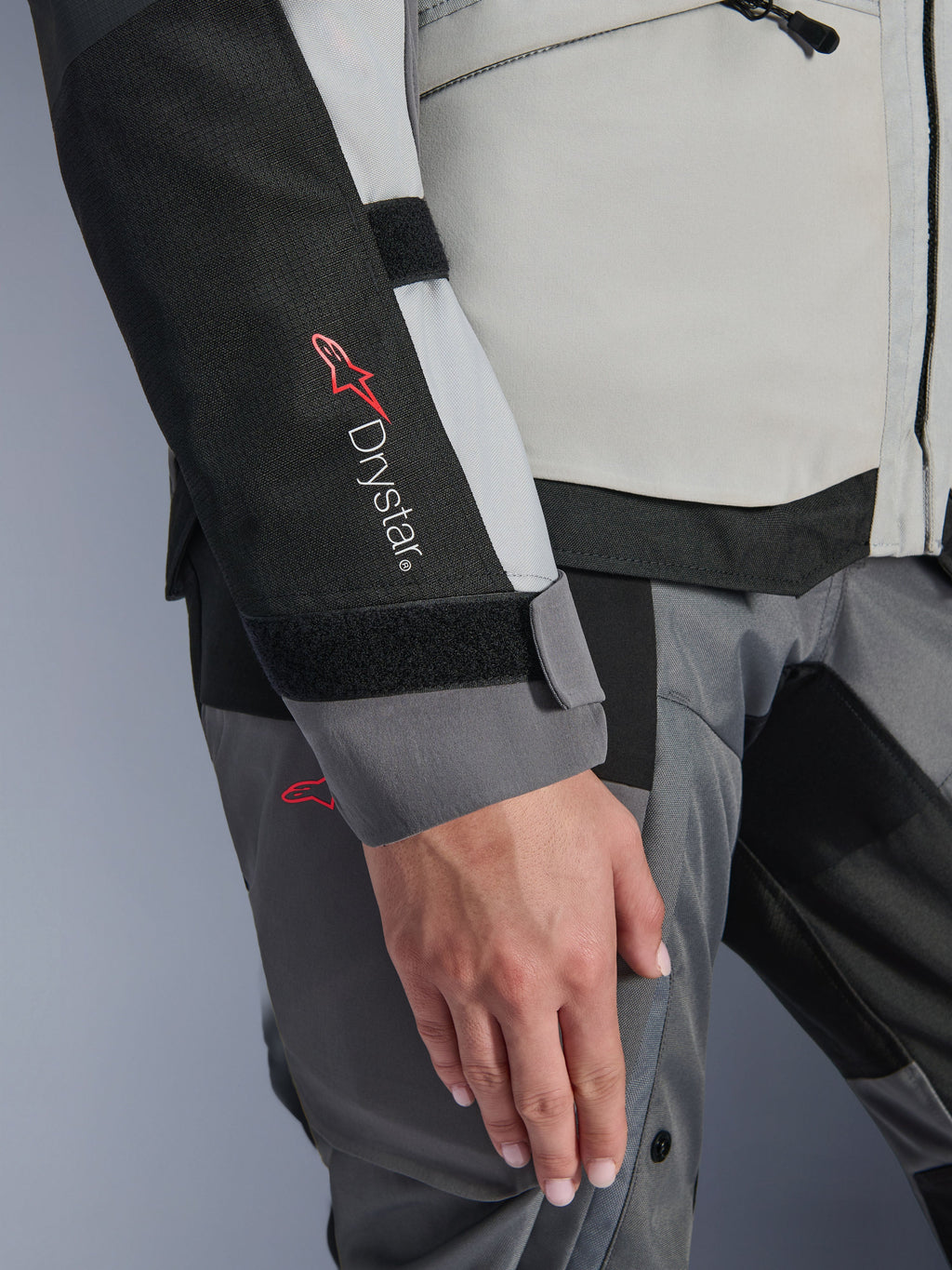 Détail en gros-plan de la veste Alpinestars Stella Andes V4 Drystar® pour femme, Gris Glacé et Gris Foncé, présentant le marquage Drystar® sur l'empiècement noir de la manche, la fermeture de poignet réglable par velcro et la construction textile robuste pour le touring d'aventure.