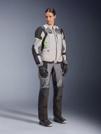Femme portant la veste Alpinestars Stella Andes V4 Drystar® et le pantalon assorti, Gris Glace et Gris Foncé avec des accents Jaune Fluo, ensemble complet d'équipement de touring aventure avec gants et bottes noirs, photo en pied en studio.