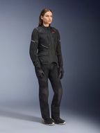 Femme portant la veste Alpinestars Stella Andes Air Drystar®, veste de touring aventure en textile noir, avec pantalon et gants noirs assortis, dotée de larges panneaux de ventilation en maille et d'un logo rouge, tenue de moto coordonnée pour femme