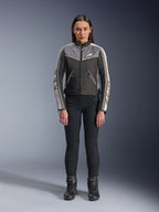 Femme portant la veste Alpinestars Stella T-Dyno WR, noir, gris foncé et écru, vue de face, veste de moto en textile au design d'inspiration vintage, avec logos sur la poitrine et les manches, portée avec un pantalon noir et des bottes