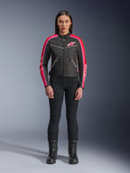 Femme portant la veste Alpinestars Stella T-Dyno WR, noire avec des accents rouge vif et fuchsia, veste textile de style vintage avec logo rose et bandes sur les manches, portée avec un pantalon noir et des bottes à lacets, équipement de moto urbain