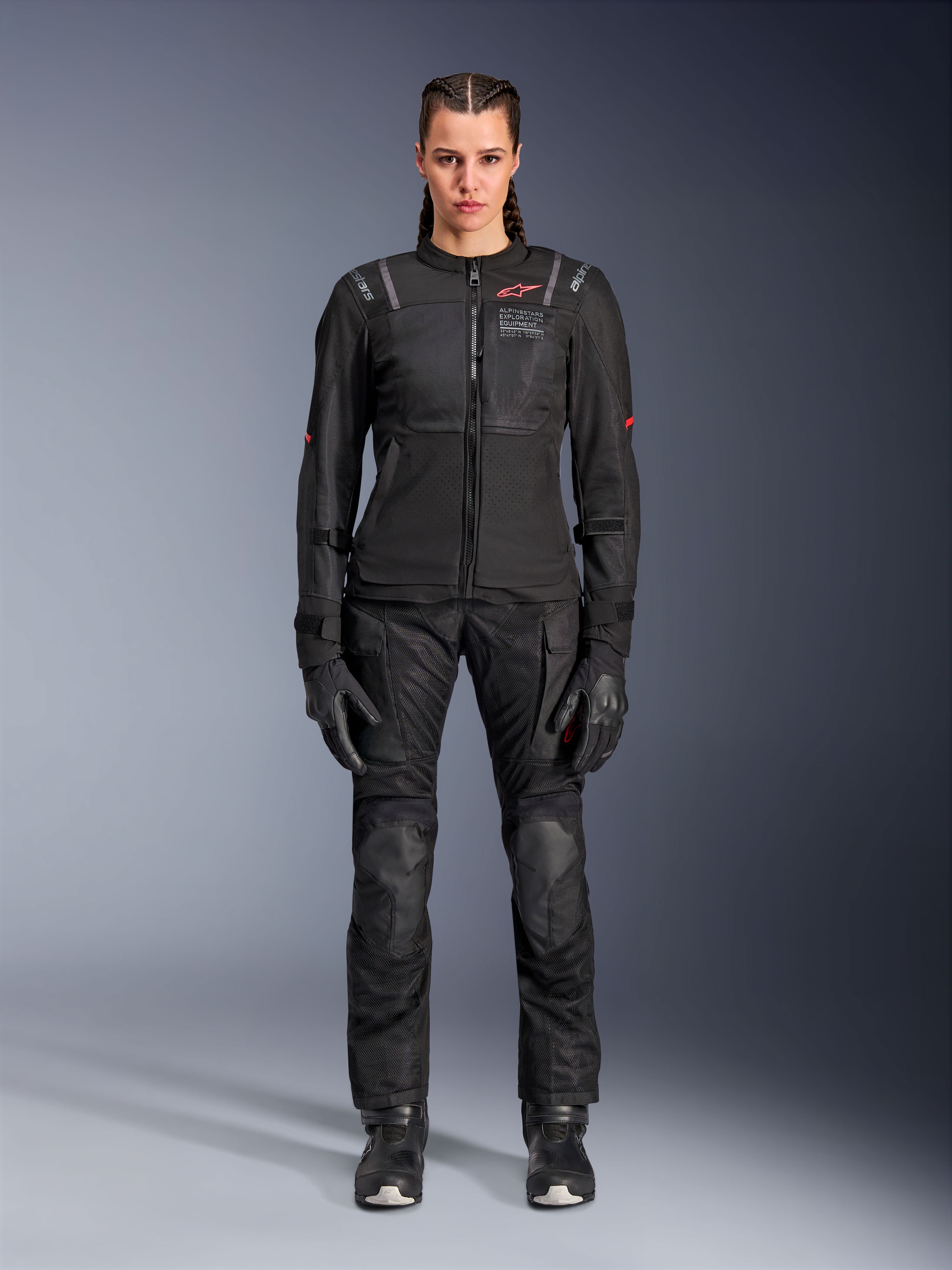 Veste Alpinestars Stella ST-2 Air, noire, vue studio en pied d'une motarde portant un pantalon et des gants de moto noirs assortis, dotée de panneaux en mesh à haute circulation d'air, de détails de logos rouges et d'un design touring moderne