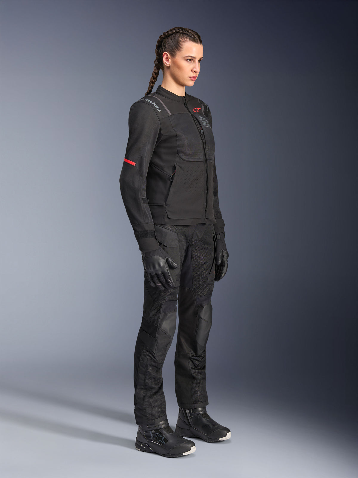 Femme pilote portant le pantalon Alpinestars Stella Andes Air Drystar® en noir, pantalon d'aventure en textile avec panneaux de ventilation en mesh, associé à une veste Stella, des gants et des bottes assortis pour une tenue de touring moto complète.