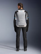 Veste Alpinestars Stella ST-2 Air, Ice Gray Black, vue arrière sur modèle féminin, avec un large panneau arrière en mesh gris clair, manches noires avec des bandes bleues, marquage Alpinestars sur le bas du dos, associée à un pantalon technique et des bottes de moto noirs, équipement de touring moto d'été