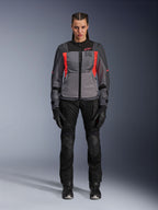 Femme portant une veste Alpinestars Stella ST-2 Air en Deep Gray, Dark Gray et Fluo Coral, associée à un pantalon et des gants de moto noirs, vue de face, équipement de touring d'aventure moderne en mesh pour femme
