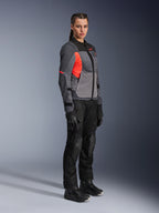 Femme motarde portant la veste Alpinestars Stella ST-2 Air en Deep Gray, Dark Gray et Fluo Coral, associée à un pantalon de moto, des gants et des bottes noirs, dotée d'un design touring moderne avec des panneaux en mesh et des détails réfléchissants.
