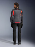 Vue arrière d'un modèle portant la veste Alpinestars Stella St-2 Air pour femme en Gris Profond et Gris Foncé avec des accents Corail Fluo, dotée de larges panneaux de ventilation en mesh dans le dos et de détails de logo réfléchissants, associée à un pantalon et des gants de moto noirs.