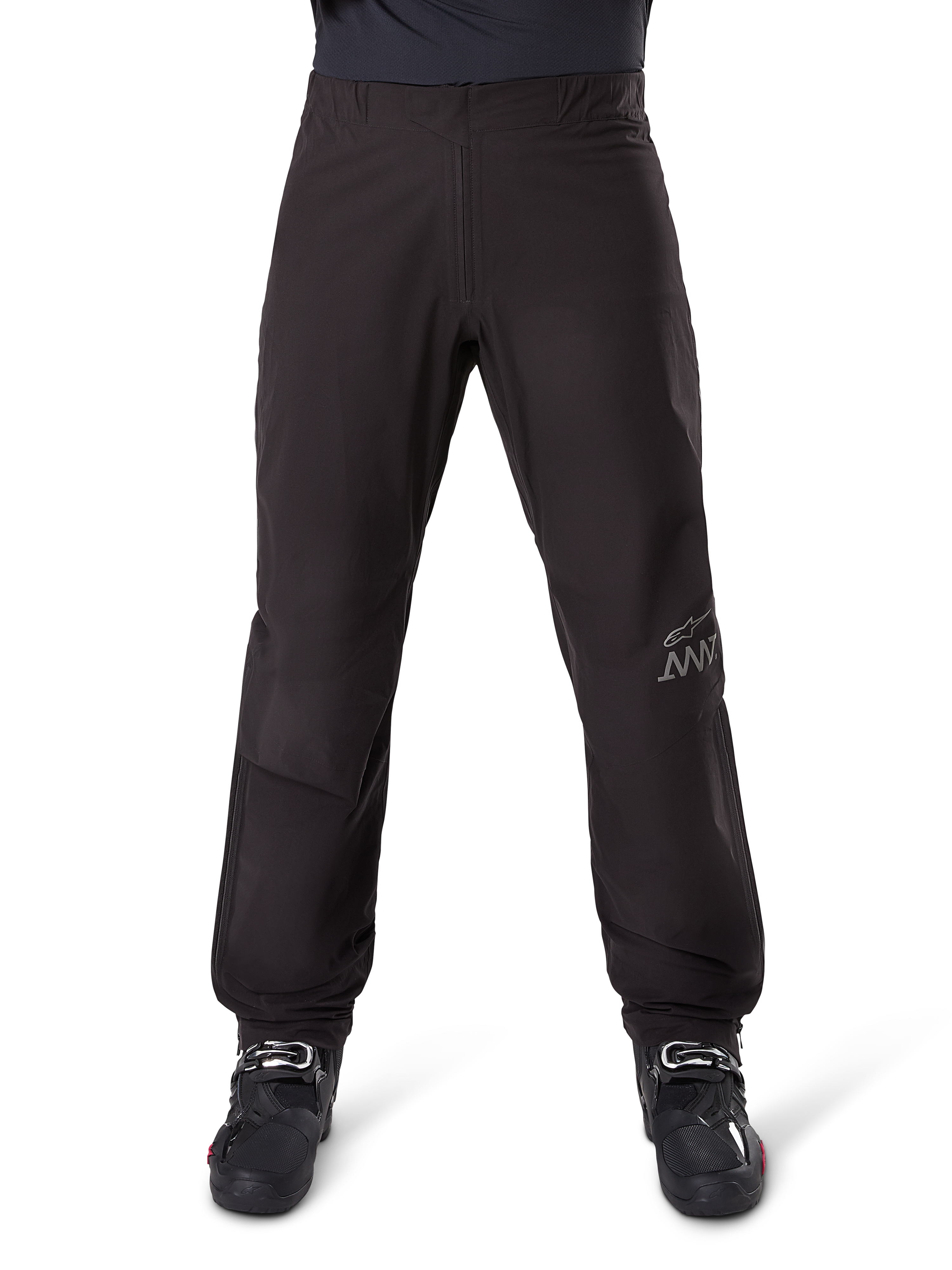 Doublure de pantalon Alpinestars AMT-8 Stretch Drystar® XF, noire, vue de face portée avec des bottes de moto noires, arborant le logo étoile gris et le marquage AMT sur la jambe, vêtement de moto polyvalent imperméable et coupe-vent
