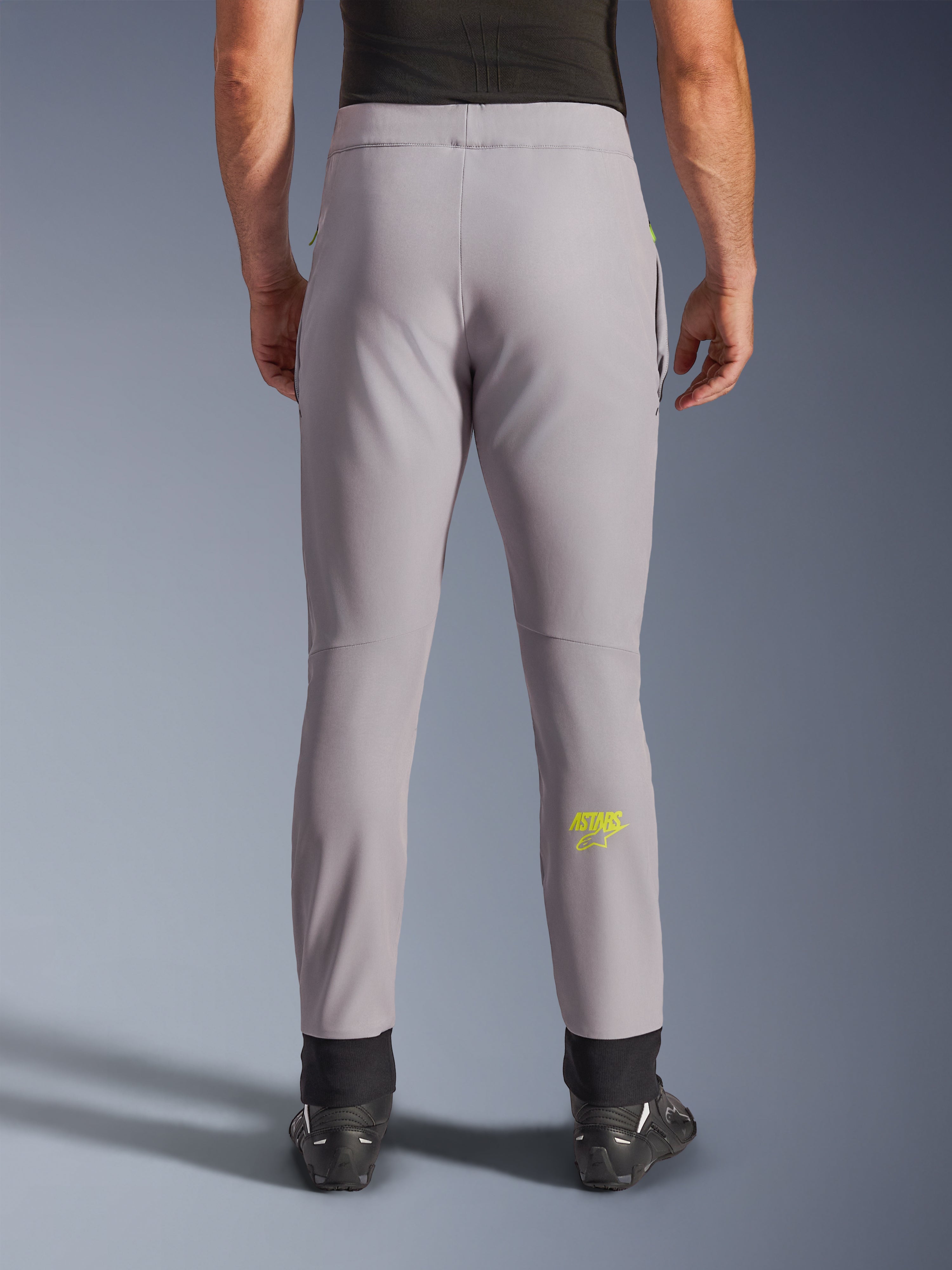 Pantalon Alpinestars Aeroshell, pantalon de moto, gris moyen et jaune fluo, vue arrière montrant le logo Astars jaune sur le mollet, chevilles élastiques noires, design moderne en textile softshell pour la route et un usage décontracté.