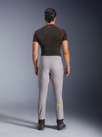 Pantalon Alpinestars Aeroshell, gris moyen avec logo jaune fluo, vue arrière d'un pantalon de moto softshell sport polyvalent, porté avec un maillot de compression noir et des chaussures de moto, doté d'une taille élastique et d'une coupe fuselée.