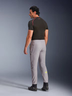 Pantalon Alpinestars Aeroshell, Mid Gray Yellow Fluo, vue de dos d'un mannequin homme portant un pantalon de moto en softshell extensible, avec le logo Astars jaune sur le mollet gauche, associé à une couche de base noire et des chaussures de moto pour une silhouette sportive moderne.