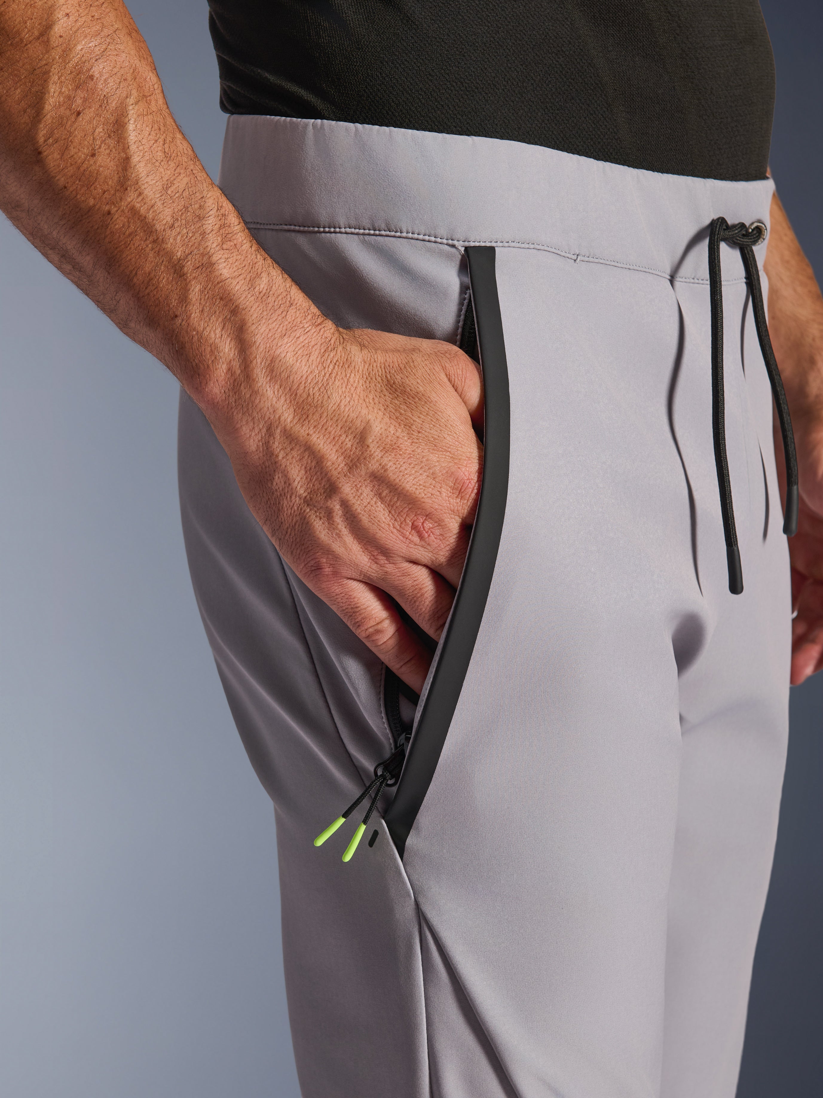 Pantalon Alpinestars Aeroshell, Gris Moyen Jaune Fluo, gros plan sur la poche avant zippée et la taille, fermeture éclair noire thermocollée avec embouts jaune fluo, taille élastique avec cordon de serrage noir, pantalon de moto softshell sport