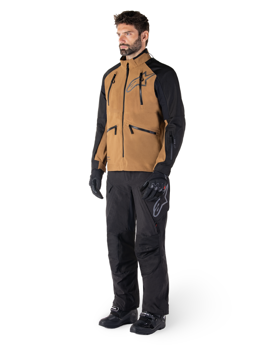 Pantalon Alpinestars Hyde XT Drystar®, pantalon de moto aventure, noir, porté avec une veste technique marron et noire, des gants et bottes noirs, doté d'une conception par-dessus la botte pour la conduite tout-terrain et dual-sport