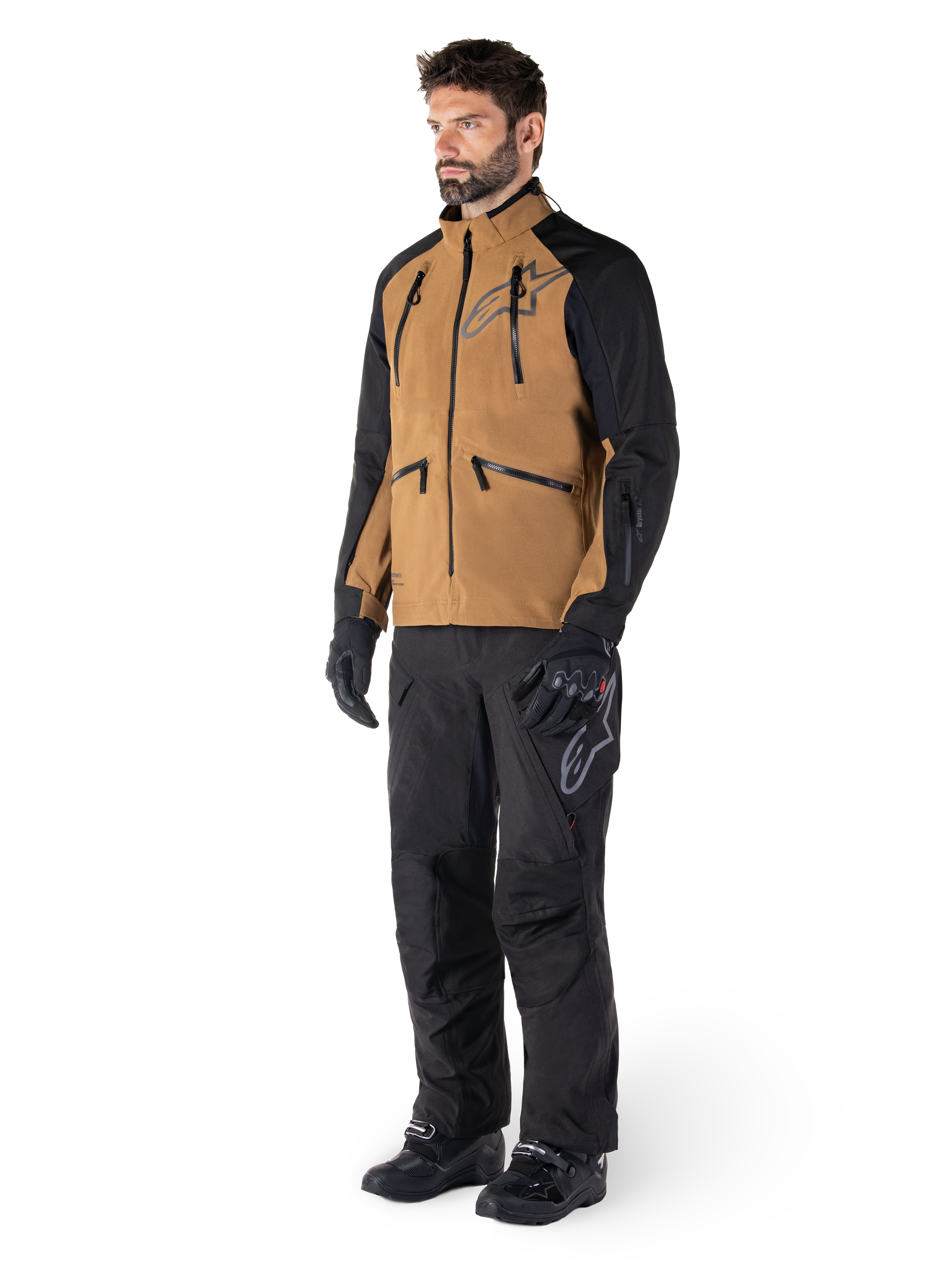 Pantalon Alpinestars Hyde XT Drystar®, pantalon de moto aventure, noir, porté avec une veste technique marron et noire, des gants et bottes noirs, doté d'une conception par-dessus la botte pour la conduite tout-terrain et dual-sport