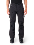 Pantalon Alpinestars Hyde XT Drystar, pantalon d'aventure touring noir, porté par un pilote avec des bottes noires, logos gris sur les cuisses, ceinture intégrée, zones de genoux renforcées et construction textile imperméable.