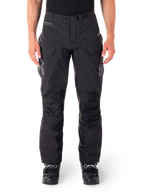Pantalon Alpinestars Hyde XT Drystar, pantalon d'aventure touring noir, porté par un pilote avec des bottes noires, logos gris sur les cuisses, ceinture intégrée, zones de genoux renforcées et construction textile imperméable.