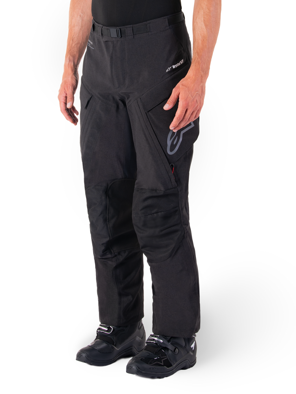 Pantalon Alpinestars Hyde XT Drystar®, pantalon de moto tourisme d'aventure, noir, porté avec des bottes noires, arborant le logo de la membrane laminée Drystar®XF, des panneaux de genoux renforcés et des poches cargo zippées.