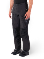 Pantalon Alpinestars Hyde XT Drystar®, pantalon de moto tourisme d'aventure, noir, porté avec des bottes noires, arborant le logo de la membrane laminée Drystar®XF, des panneaux de genoux renforcés et des poches cargo zippées.