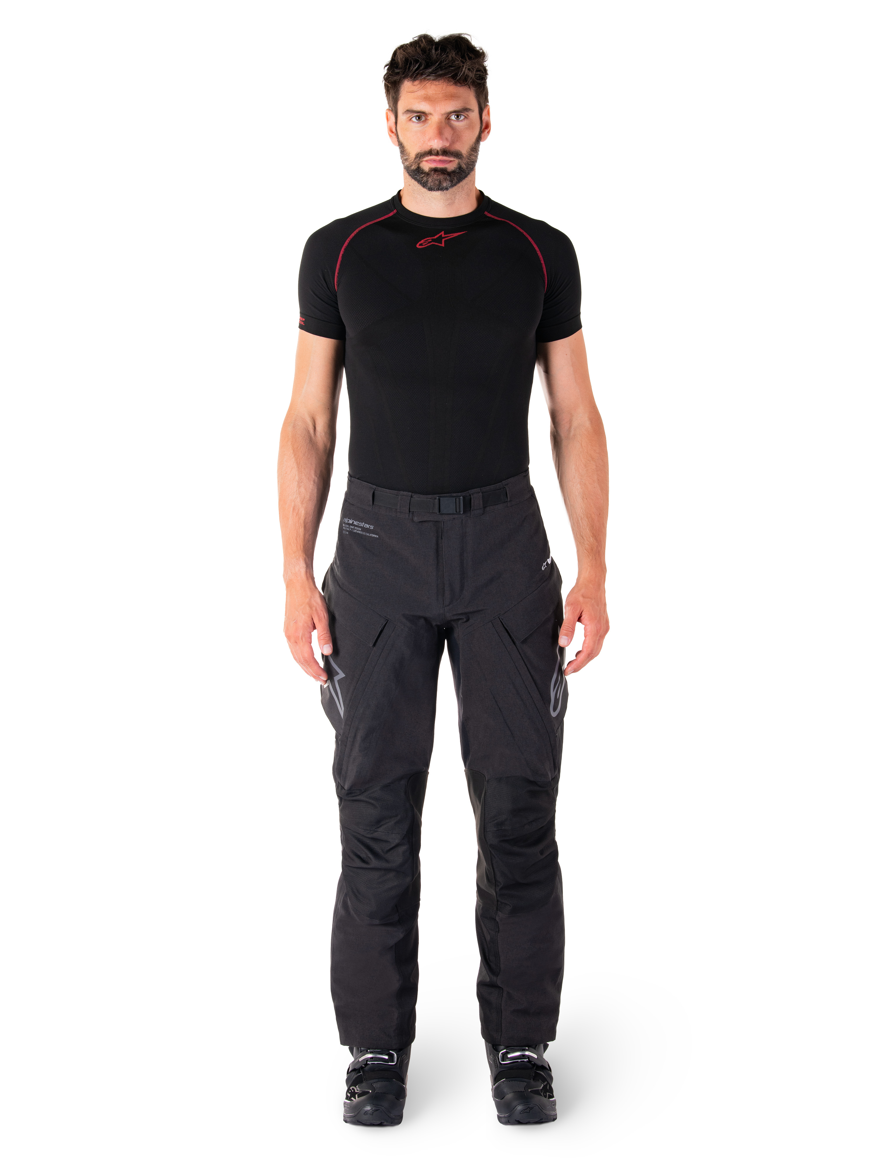 Pantalon Alpinestars Hyde XT Drystar®, pantalon de moto Adventure Touring, noir, porté par un mannequin avec une couche de base noire à manches courtes et des bottes noires, doté d'une matière extensible technique, de panneaux de genoux renforcés et de poches cargo ergonomiques.