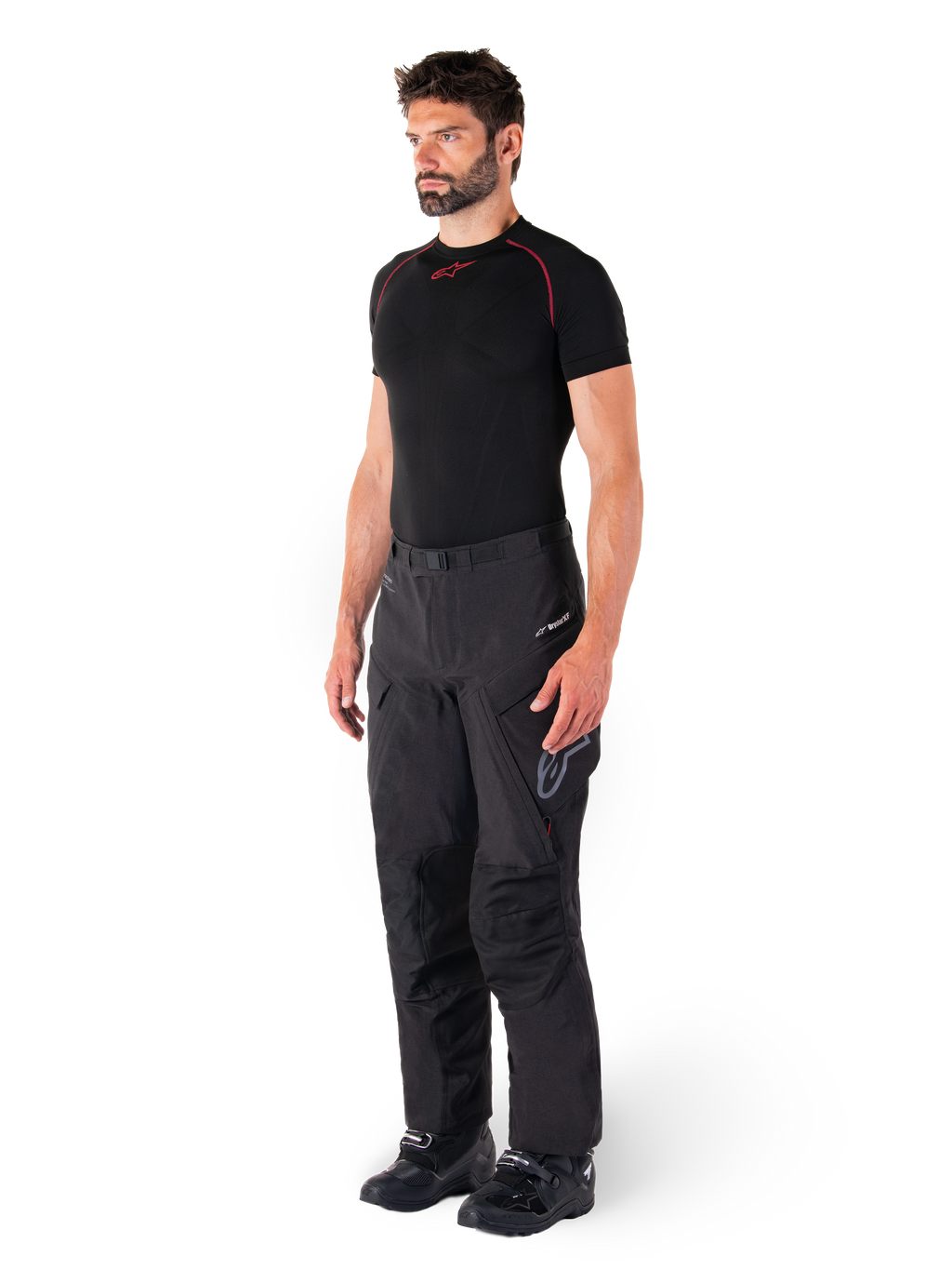 Pantalon Alpinestars Hyde XT Drystar®, pantalon de moto de tourisme d'aventure noir porté par un mannequin avec un maillot de compression noir et des bottes noires, doté d'une construction technique imperméable et du logo Drystar®XF