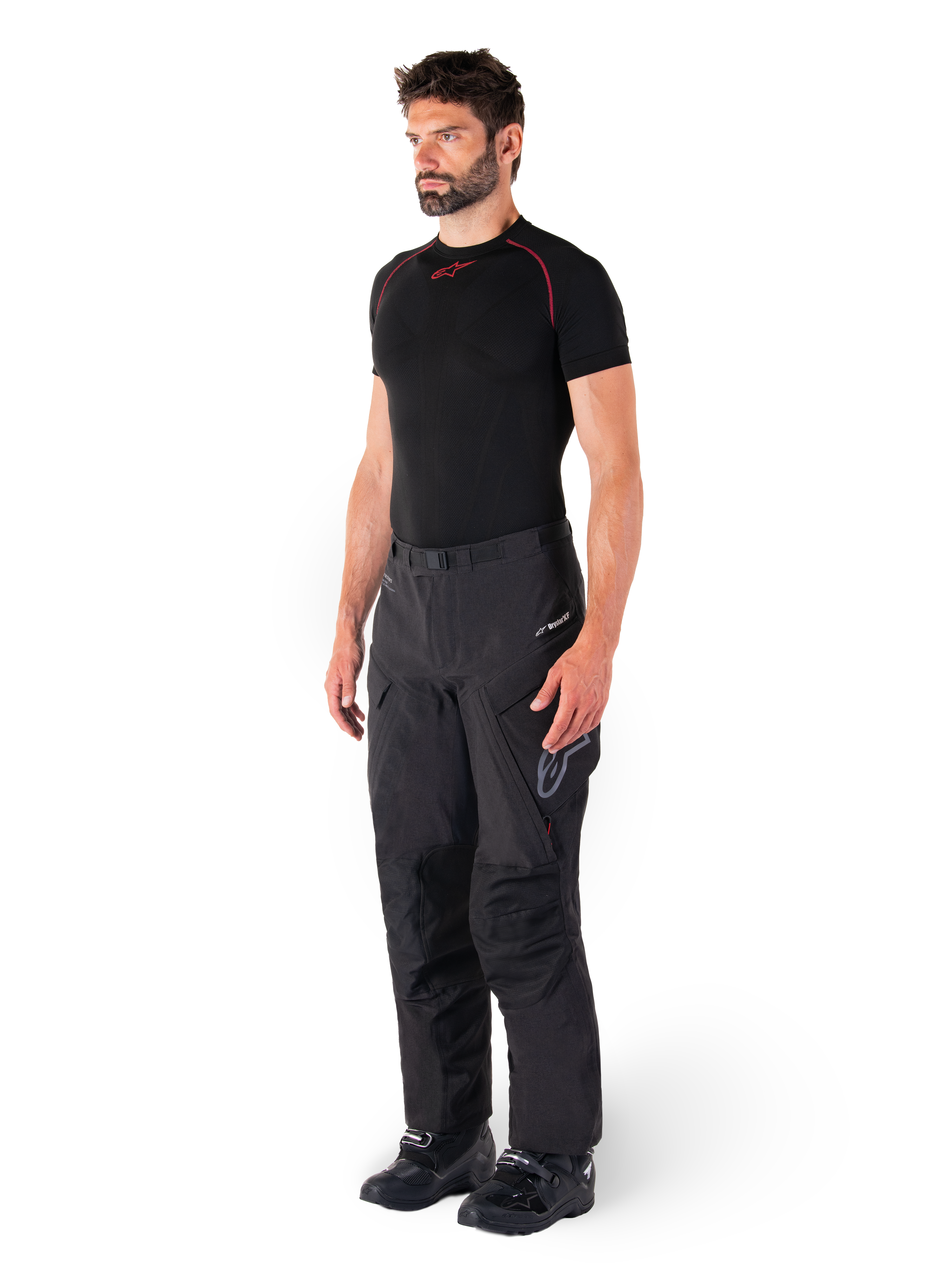 Pantalon Alpinestars Hyde XT Drystar®, pantalon de moto de tourisme d'aventure noir porté par un mannequin avec un maillot de compression noir et des bottes noires, doté d'une construction technique imperméable et du logo Drystar®XF