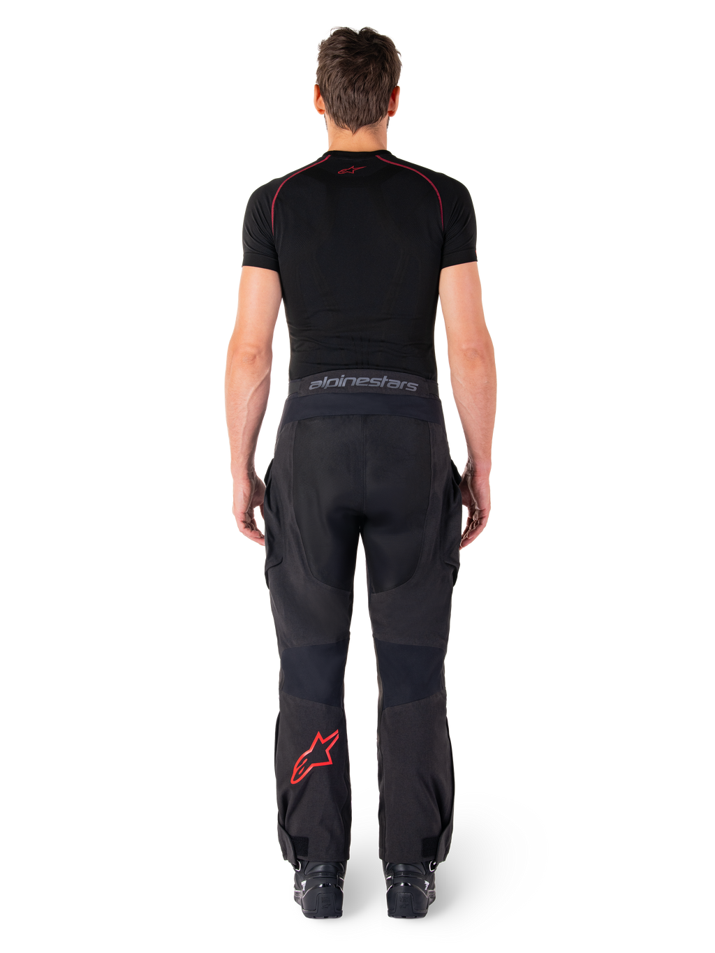 Pantalon Alpinestars Hyde XT Drystar®, pantalon de moto Adventure Touring, noir et rouge vif, vue arrière d'un pilote portant le pantalon et une couche de base noire, avec un logo étoile rouge sur la jambe gauche et un marquage gris sur la ceinture.