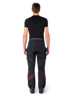 Pantalon Alpinestars Hyde XT Drystar®, pantalon de moto Adventure Touring, noir et rouge vif, vue arrière d'un pilote portant le pantalon et une couche de base noire, avec un logo étoile rouge sur la jambe gauche et un marquage gris sur la ceinture.