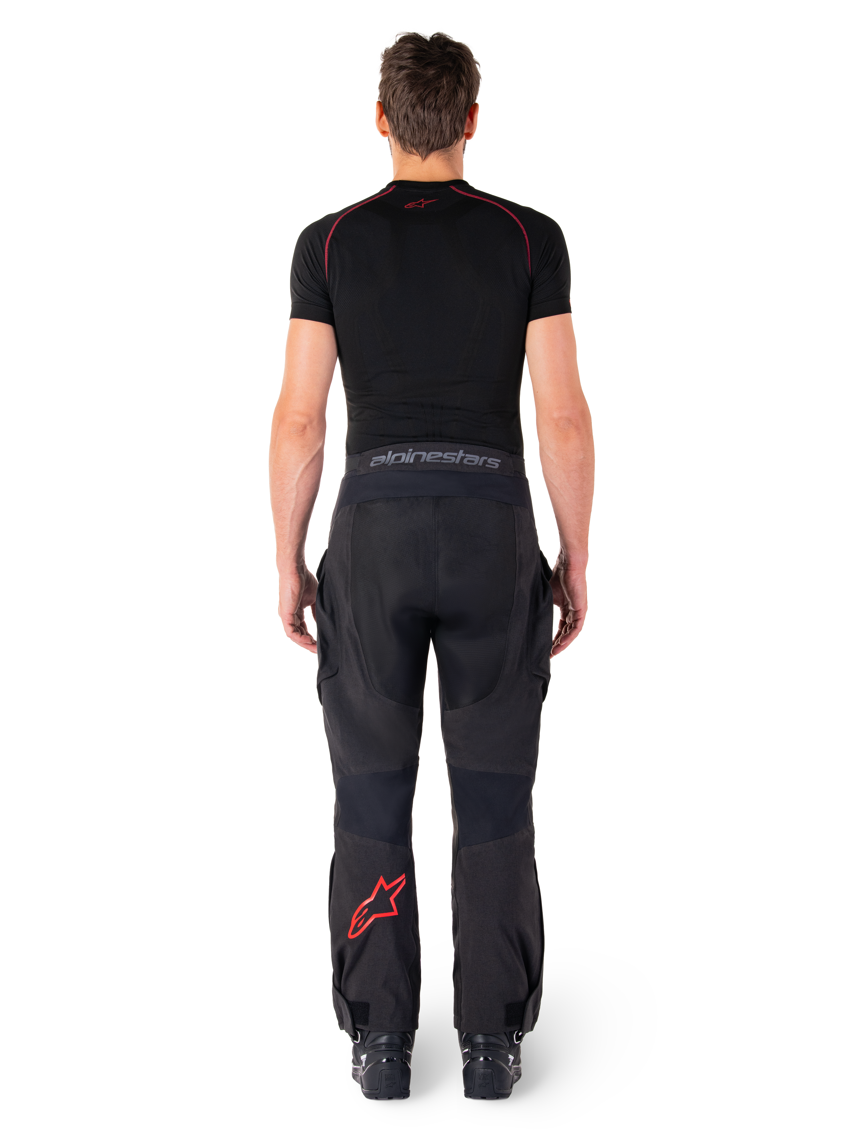 Pantalon Alpinestars Hyde XT Drystar®, pantalon de moto Adventure Touring, noir et rouge vif, vue arrière d'un pilote portant le pantalon et une couche de base noire, avec un logo étoile rouge sur la jambe gauche et un marquage gris sur la ceinture.