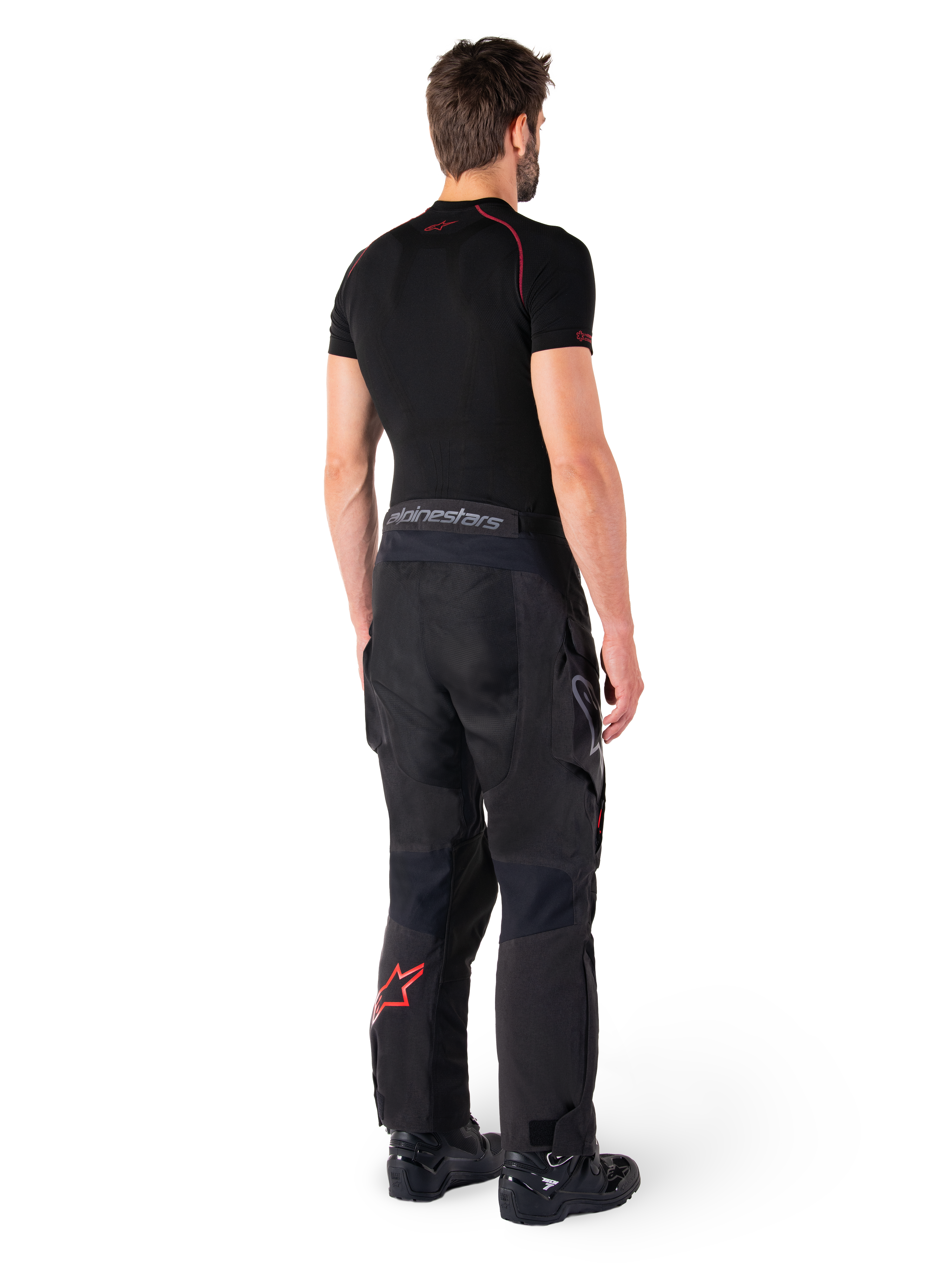 Pantalon Alpinestars Hyde XT Drystar®, pantalon d'aventure touring, noir et rouge vif, vue arrière d'un pilote portant le pantalon avec une sous-couche noire et des bottes noires, doté d'une construction textile durable avec un logo étoile rouge sur le bas de la jambe et le marquage Alpinestars gris sur la ceinture