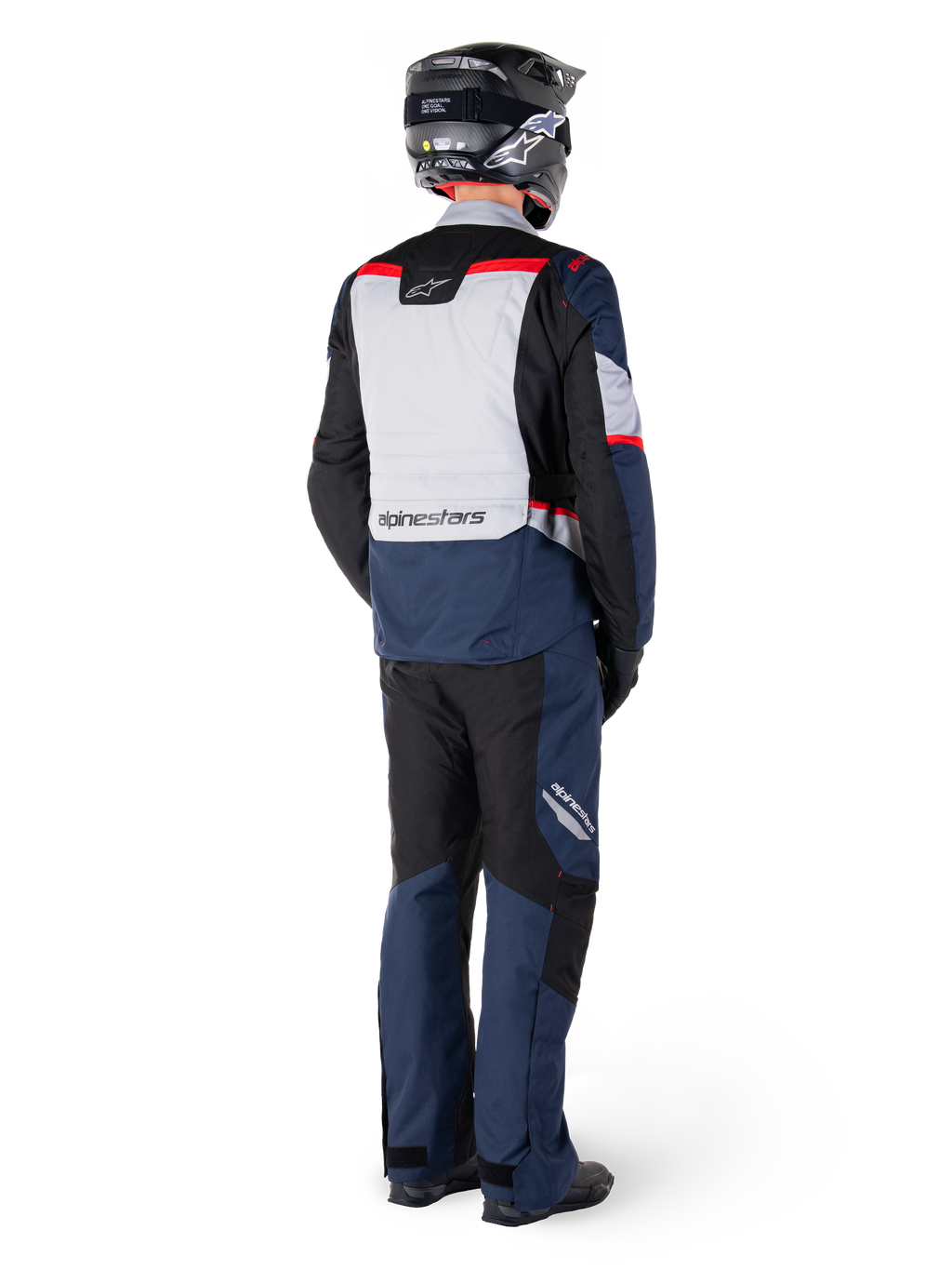 Vue arrière d'un motard portant un pantalon imperméable Alpinestars ST-1 et une veste assortie en Bleu Foncé, Noir et Rouge Vif, équipement de touring aventure avec panneaux textiles et détails réfléchissants, associé à un casque et des bottes noirs