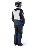 Vue arrière d'un motard portant un pantalon imperméable Alpinestars ST-1 et une veste assortie en Bleu Foncé, Noir et Rouge Vif, équipement de touring aventure avec panneaux textiles et détails réfléchissants, associé à un casque et des bottes noirs
