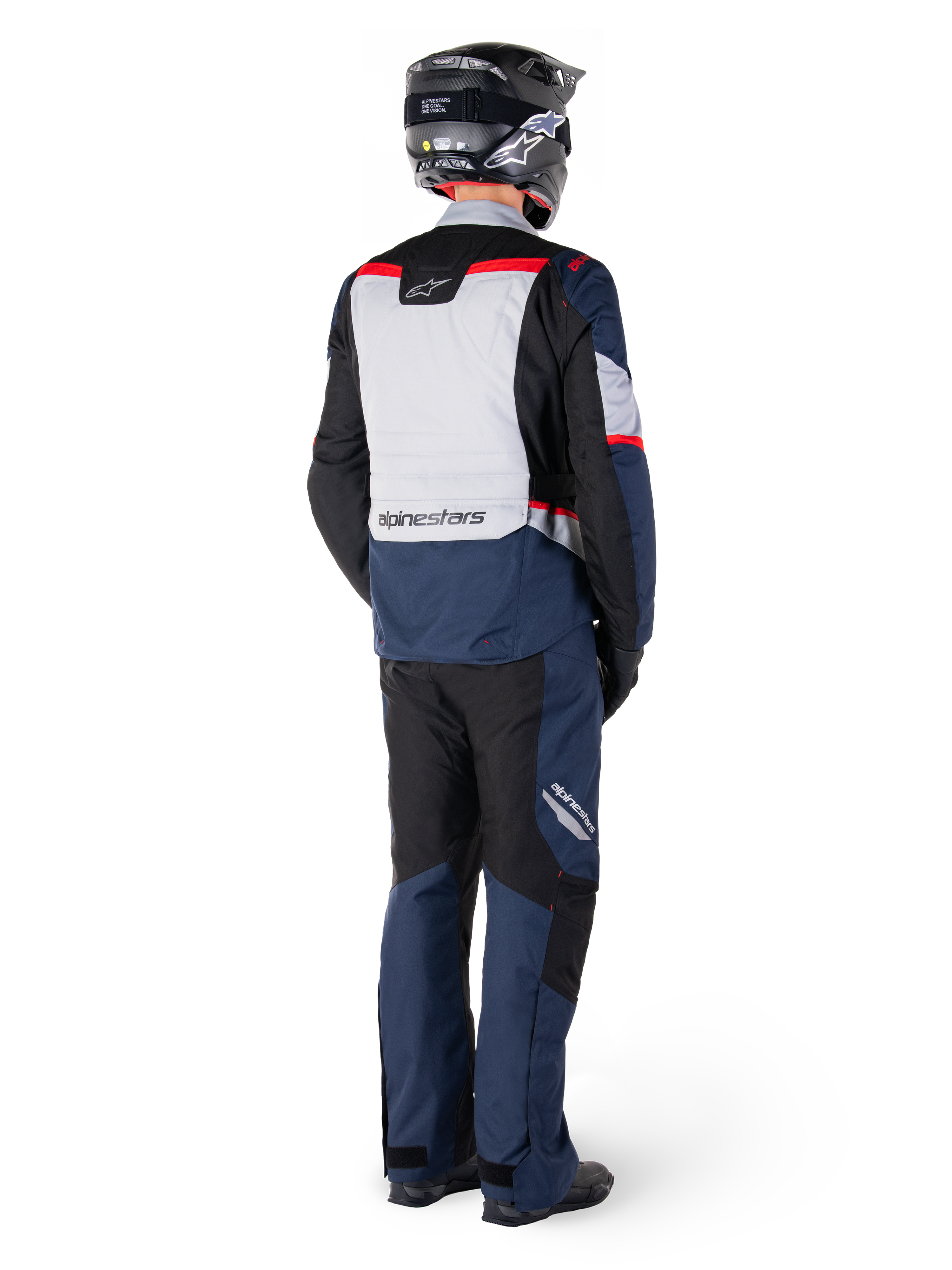 Vue arrière d'un motard portant un pantalon imperméable Alpinestars ST-1 et une veste assortie en Bleu Foncé, Noir et Rouge Vif, équipement de touring aventure avec panneaux textiles et détails réfléchissants, associé à un casque et des bottes noirs
