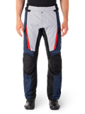 Alpinestars ST-1 Waterproof Pants, pantalon de moto touring, bleu foncé et gris clair avec des accents rouge vif, empiècements renforcés noirs aux genoux, vue de face porté avec des bottes noires, équipement de touring aventure imperméable