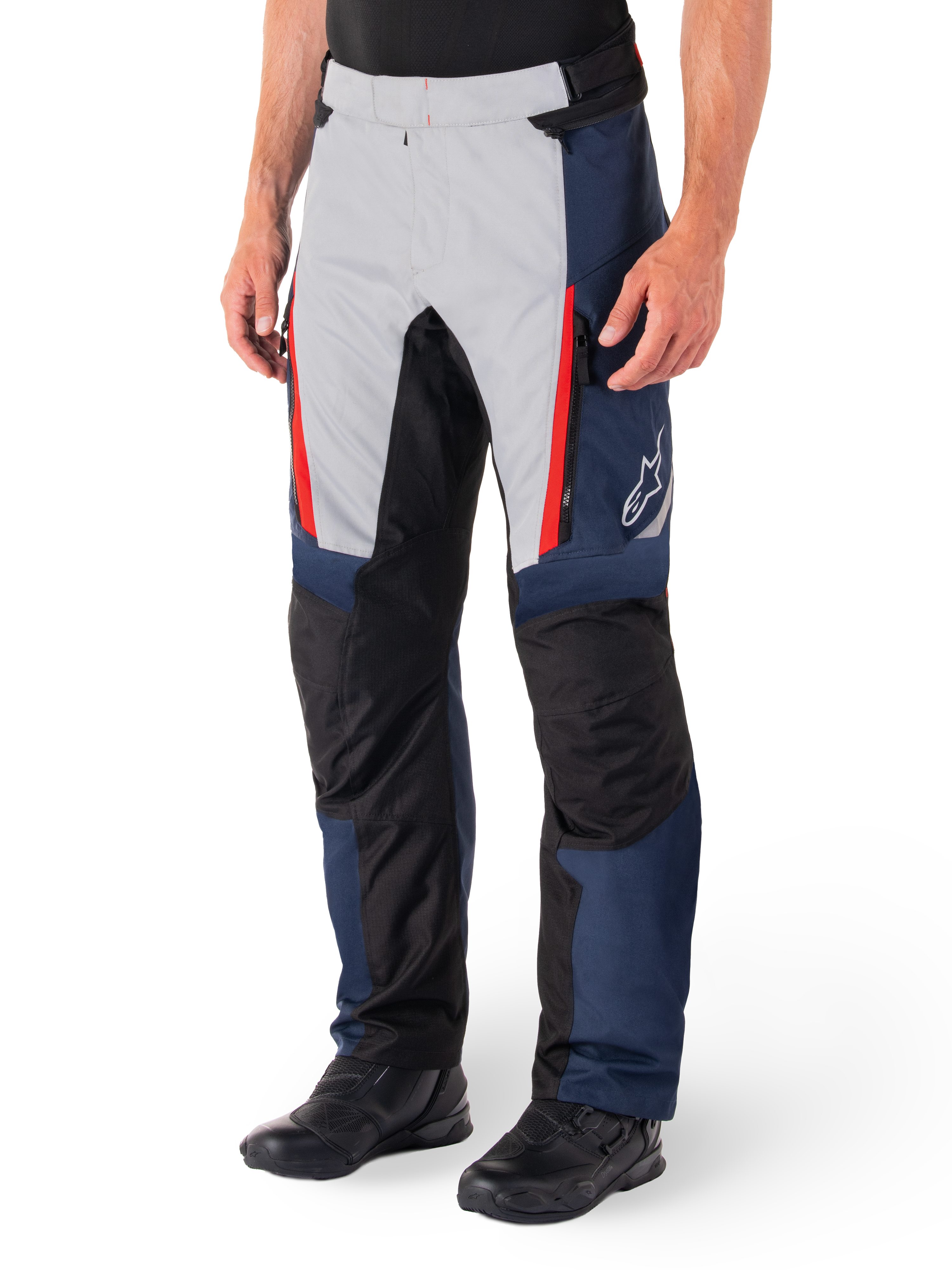 Pantalon imperméable Alpinestars St-1, pantalon de moto touring, bleu foncé, noir et rouge vif, comprenant des panneaux avant gris clair avec des fermetures éclair rouges, des renforts noirs aux genoux et un logo Alpinestars blanc sur le côté, porté avec des bottes de moto noires.