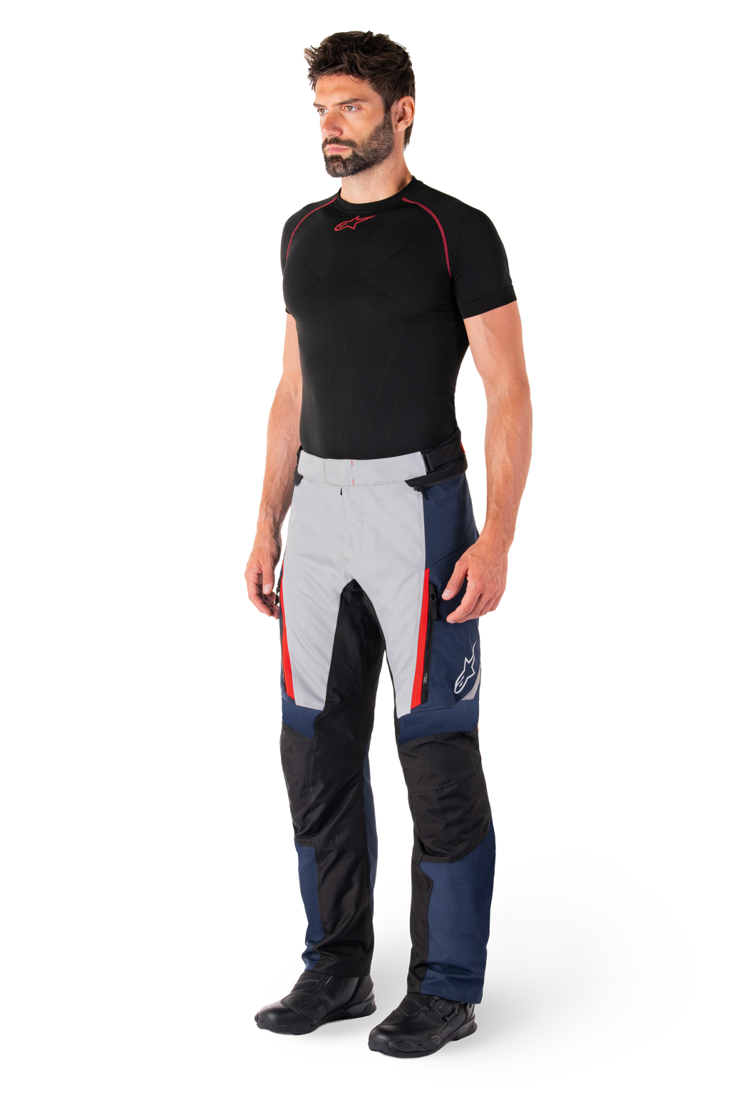 Pantalon imperméable Alpinestars St-1, pantalon de moto touring, bleu foncé, noir et rouge vif, porté par un mannequin avec une couche de base noire et des bottes noires, doté de poches zippées et du logo Alpinestars sur la jambe