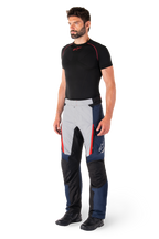 Pantalon imperméable Alpinestars St-1, pantalon de moto touring, bleu foncé, noir et rouge vif, porté par un mannequin avec une couche de base noire et des bottes noires, doté de poches zippées et du logo Alpinestars sur la jambe