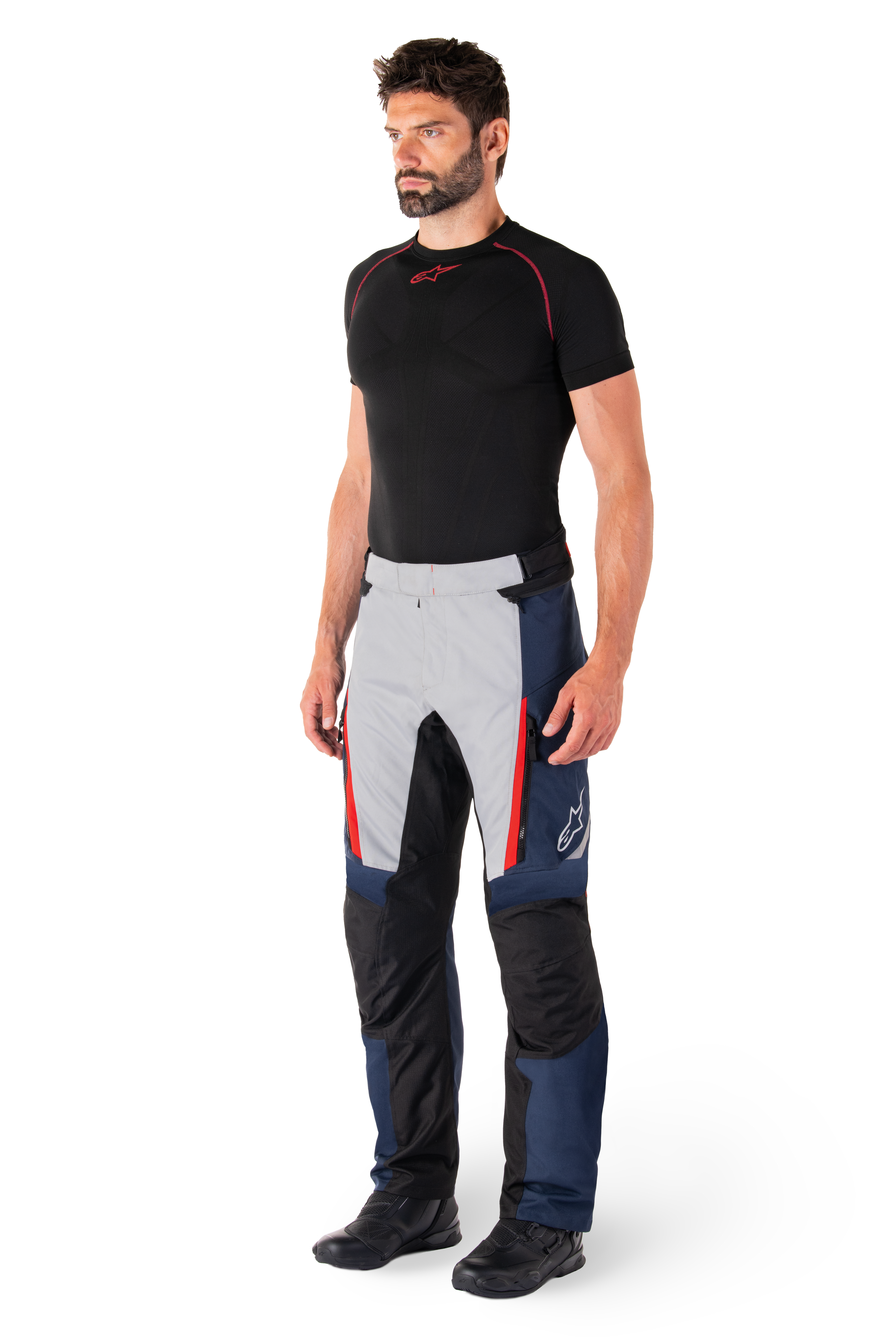 Pantalon imperméable Alpinestars St-1, pantalon de moto touring, bleu foncé, noir et rouge vif, porté par un mannequin avec une couche de base noire et des bottes noires, doté de poches zippées et du logo Alpinestars sur la jambe