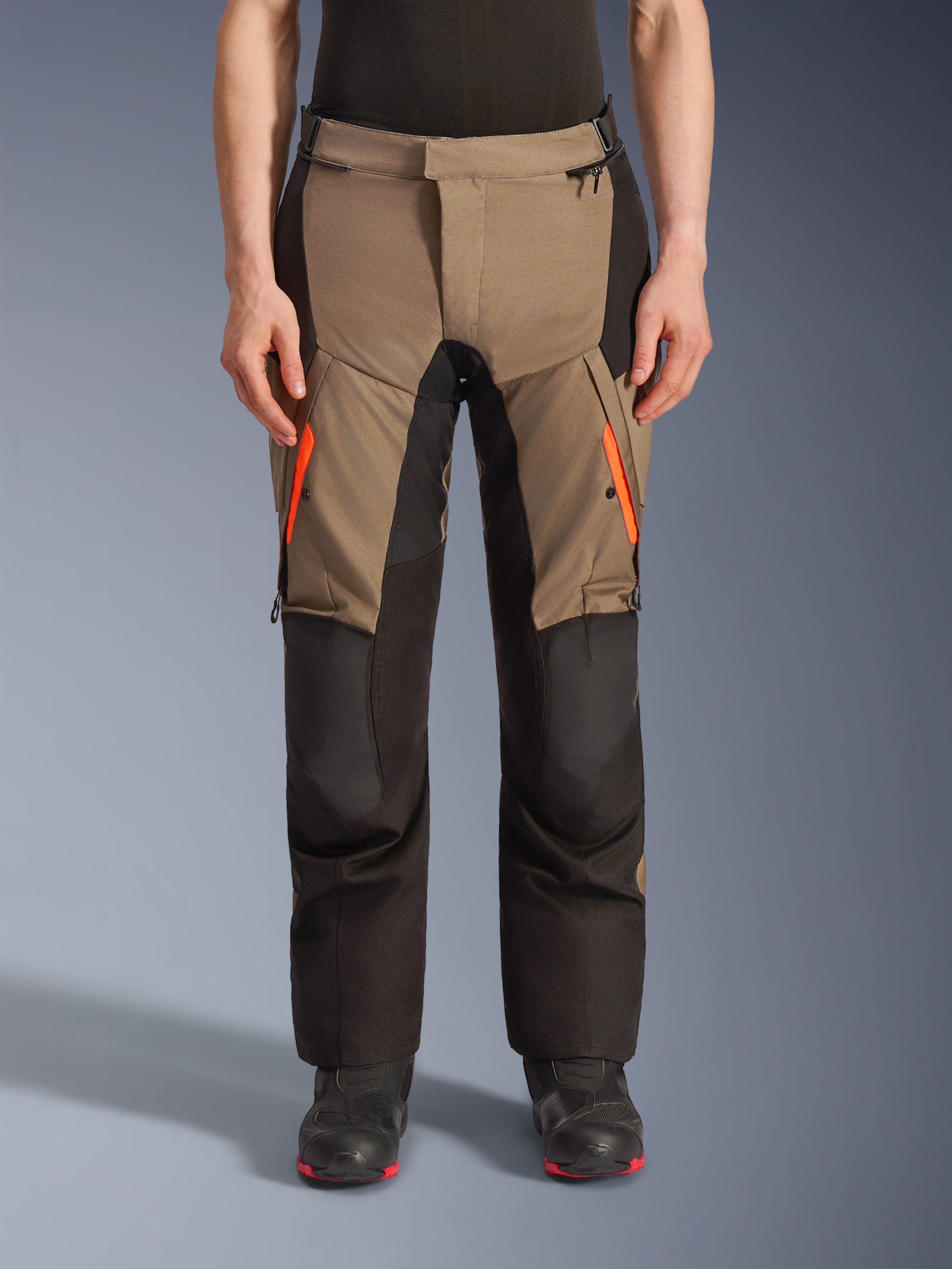 Alpinestars Andes V4 Drystar® Pants, pantalon de moto adventure touring marron et noir, doté de fermetures éclair orange vif sur les cuisses, de panneaux de genoux noirs renforcés et d'une construction textile robuste pour rouler par tous les temps.