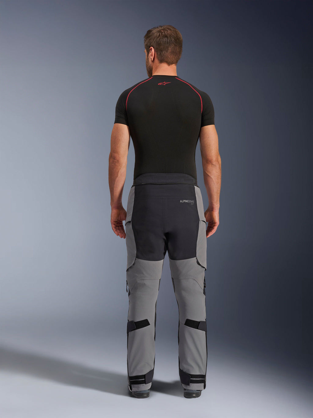 Pantalon Alpinestars Andes Pro Drystar® XF, pantalon de moto adventure, gris foncé et noir, vue arrière montrant la construction à panneaux gris et noirs, porté avec une couche de base noire, doté d'une assise renforcée et de sangles de réglage aux mollets pour le touring.
