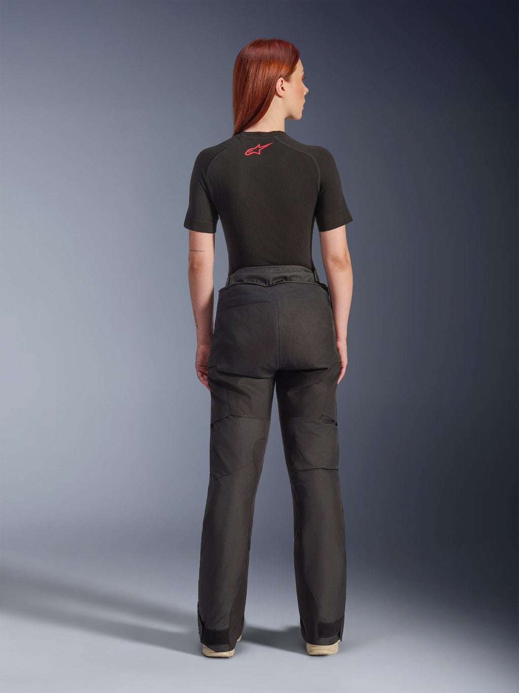 Vue arrière d'un mannequin portant le pantalon Alpinestars Stella Andes V4 Drystar® noir, associé à une sous-couche noire à manches courtes ornée d'un logo Alpinestars rouge, équipement de moto d'aventure-touring avec une construction textile durable.