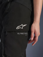 Alpinestars Stella Andes V4 Drystar®, pantalon de moto pour femme, noir, gros plan sur la poche cargo de la cuisse avec logo étoile blanc et marquage, matériau textile résistant pour le touring d'aventure