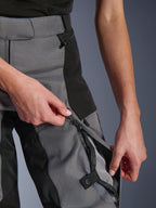 Pantalon Alpinestars Stella Andes V4 Drystar® pour femme, noir et gris foncé, gros plan de mains ouvrant la ventilation zippée sur la cuisse pour révéler une maille respirante, fermetures éclair étanches, construction textile durable pour le pilotage d'aventure