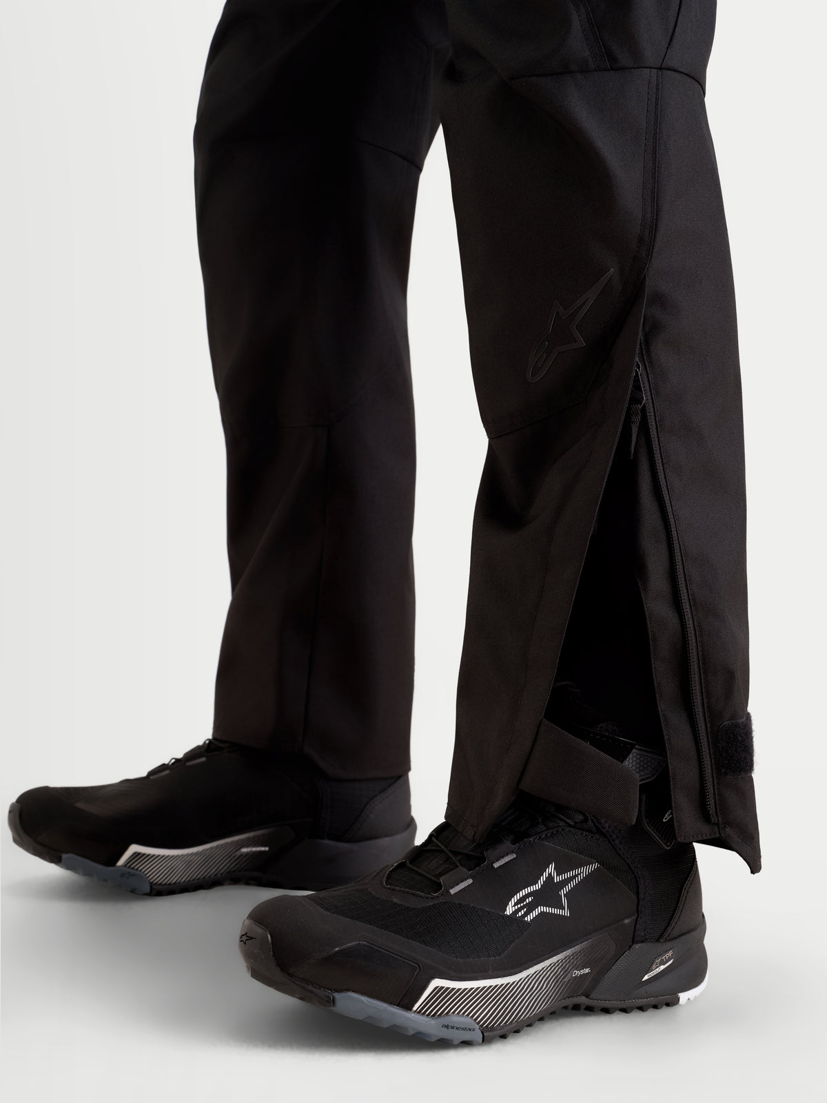 Alpinestars Stella C-1 Waterproof Pants, women's urban contemporary motorcycle pants in black, close-up view showing extended lower leg openings with zippered gussets worn over riding footwear.