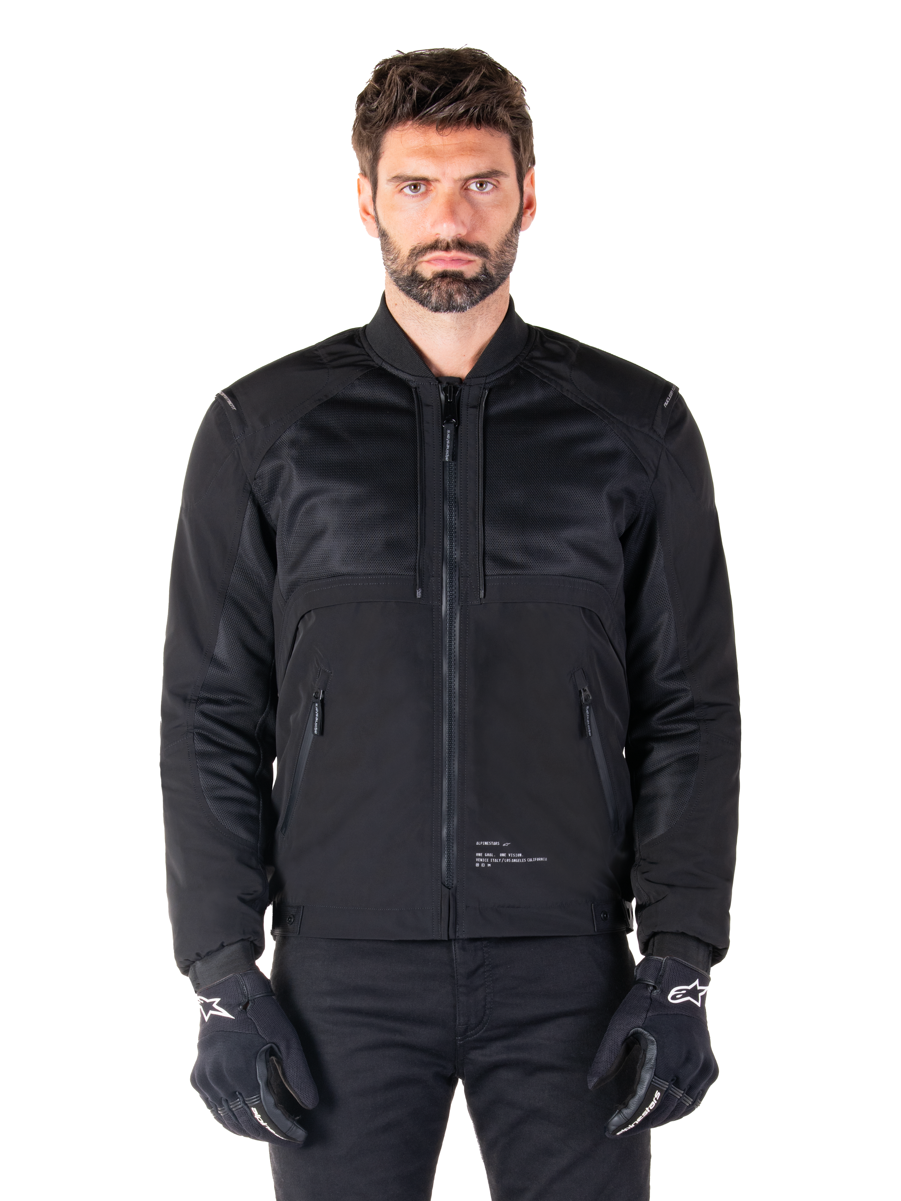 Alpinestars Mootant Waterproof Parka, Black motorcycle jacket, Front view on male model, featuring modular textile construction with mesh panels for ventilation, ribbed collar, and zippered pockets, worn with black gloves with white Alpinestars branding